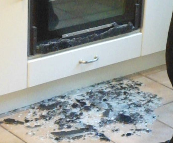 The front of an oven, with a pile of tempered glass shards on the floor beneath it.