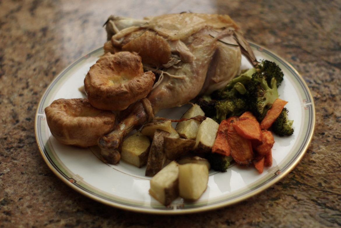 A plate of thanksgiving food, with a turkey leg, Yorkshire Puddings, broccoli, carrots and potatoes.