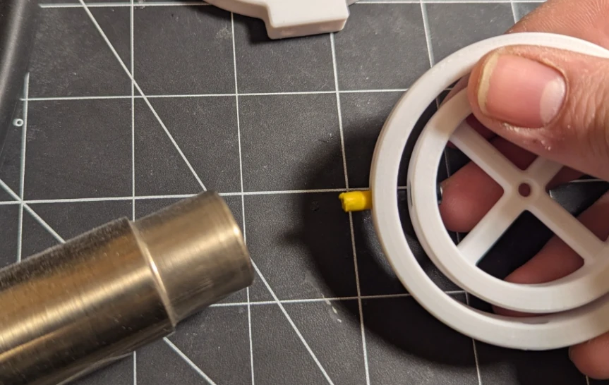 A heat gun is shown warming the side of a 3d printed part where the BIC pencil pivot is to be inserted.