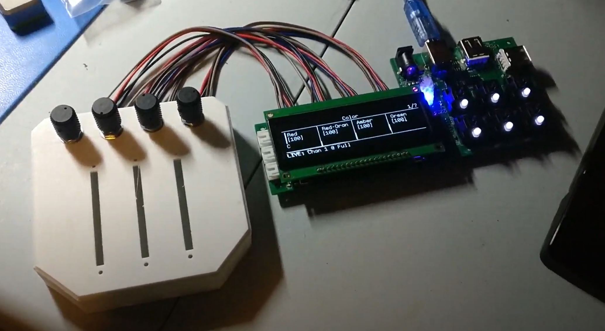 An L shaped PCB with a screen attached, connected to a panel with four rotary encoders. Information about a stage light is displayed on the screen.